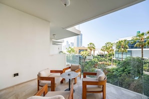 A balcony with a seating area, a glass railing, and a view of a cityscape and greenery. - Modern 2BR Gem | Prime Palm Jumeirah Location (Dubai)