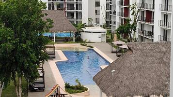 A swimming pool with a slide, surrounded by buildings with balconies, and a tennis court.