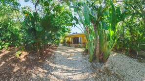 A tropical garden with a yellow building, gravel path, and various green plants. - Charming Villa with Access to the Yalku Lagoon (Akumal)