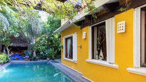A yellow building with a swimming pool, surrounded by lush greenery and a thatched-roof structure. - Vrbo Property (Unknown)