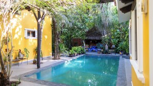 A swimming pool surrounded by lush greenery and a yellow building. - Vrbo Property (Unknown)