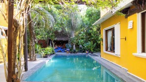 A swimming pool surrounded by lush greenery and a yellow building. - A charming villa with access to Yalku Lagoon (Akumal)