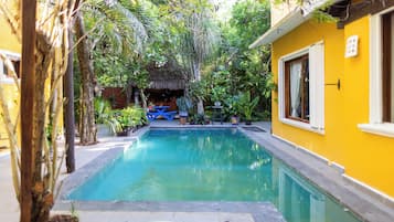 A swimming pool surrounded by lush greenery and a yellow building.