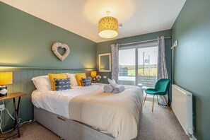 A bedroom with a bed, a chair, a lamp, a heater, and a view of the outdoors. - 1 Bed in Gatehouse Of Fleet (oc-t34445) (Gatehouse of Fleet)