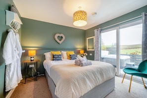 A bedroom with a bed, bedside lamps, a heart-shaped wall decoration, a window with a view, and a green chair. - 1 Bed in Gatehouse Of Fleet (oc-t34445) (Gatehouse of Fleet)