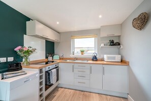 A compact kitchen with a microwave, kettle, and a window with a view. - 1 Bed in Gatehouse Of Fleet (oc-t34445) (Gatehouse of Fleet)