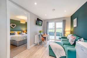 A modern room with a bed, a green sofa, a dining table, and a TV mounted on the wall. - 1 Bed in Gatehouse Of Fleet (oc-t34445) (Gatehouse of Fleet)