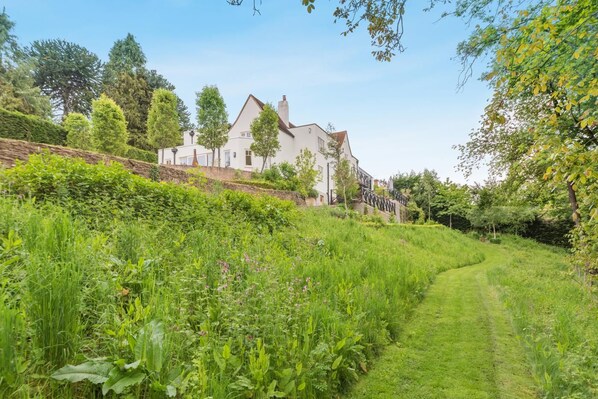 A white building with a sloped roof, surrounded by lush greenery and a clear sky. - 5 Bed in Devizes (oc-s34742) (Devizes)