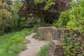 A gravel path leading through a garden with stone walls and various plants.