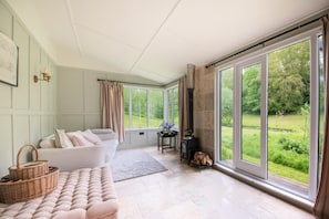 A room with a sofa, a table with a vase, a fireplace, and large windows with a view of greenery. - 5 Bed in Devizes (oc-s34742) (Devizes)