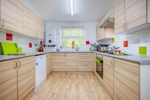 A modern kitchen with wooden cabinets, a dishwasher, and a window with blinds. - 2 Bed in Swanage (oc-t35179) (Swanage)