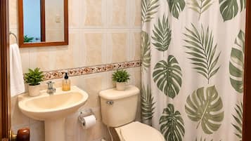 Un baño con lavamanos, inodoro y cortina de ducha con estampado de hojas tropicales.