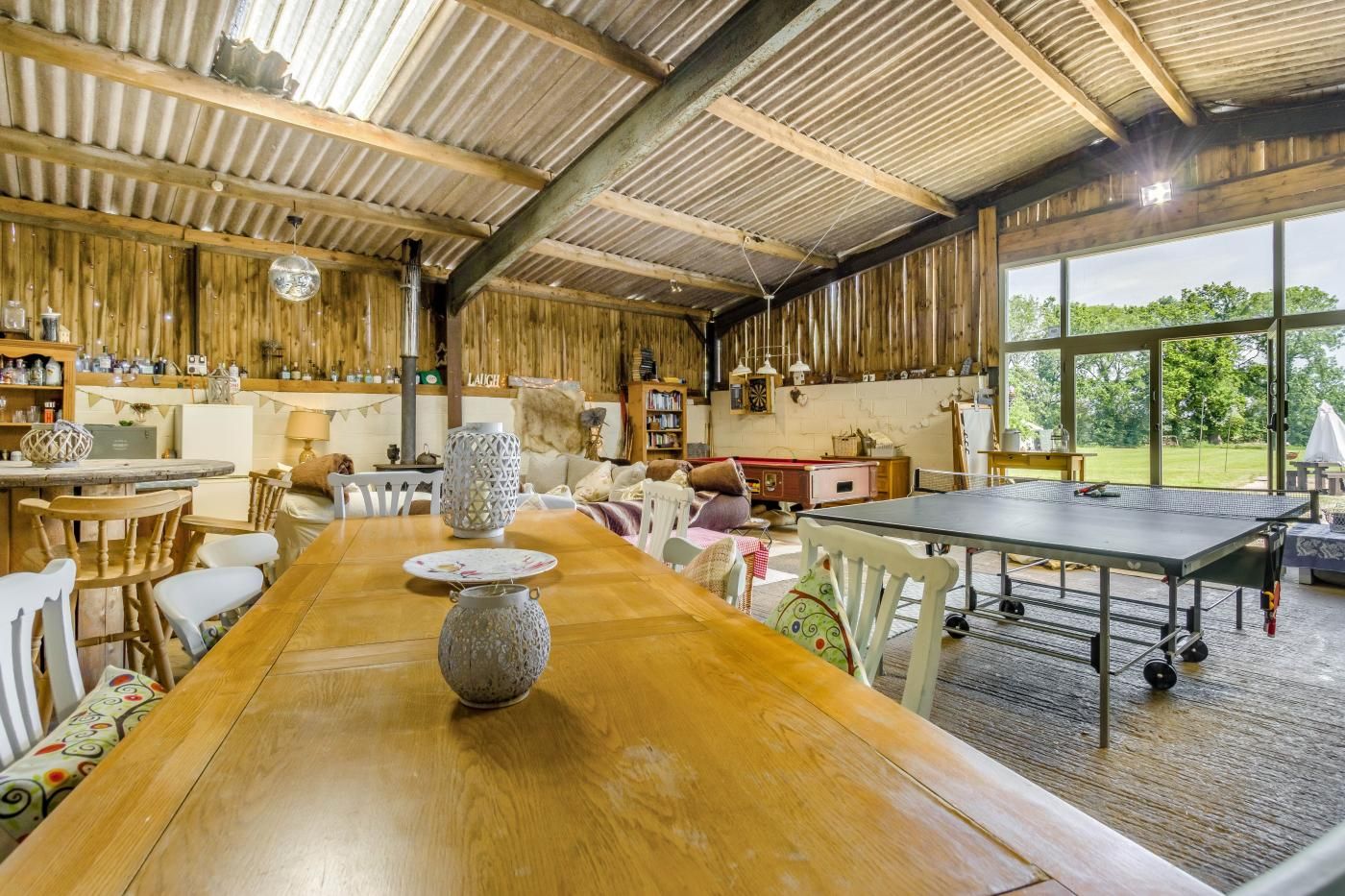 Un intérieur rustique avec une longue table en bois, une table de ping-pong et différentes étagères remplies d’objets.
