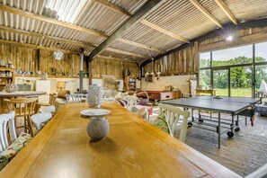 Ein rustikales Interieur mit einem langen Holztisch, einem Tischtennisschrank und verschiedenen Regalen mit Gegenständen.
