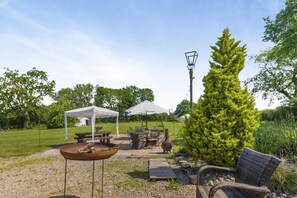 An outdoor patio area with a table, chairs, a gazebo, and a tall coniferous tree.