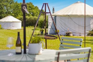 A rustic outdoor setting with a table, chairs, a hanging chair, and yurts in the background.