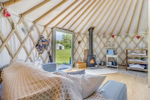 Ein gemütliches Zeltinneres mit Kamin in der Mitte, einer Sitzecke mit Kissen und einem kleinen Tisch mit Gegenständen.