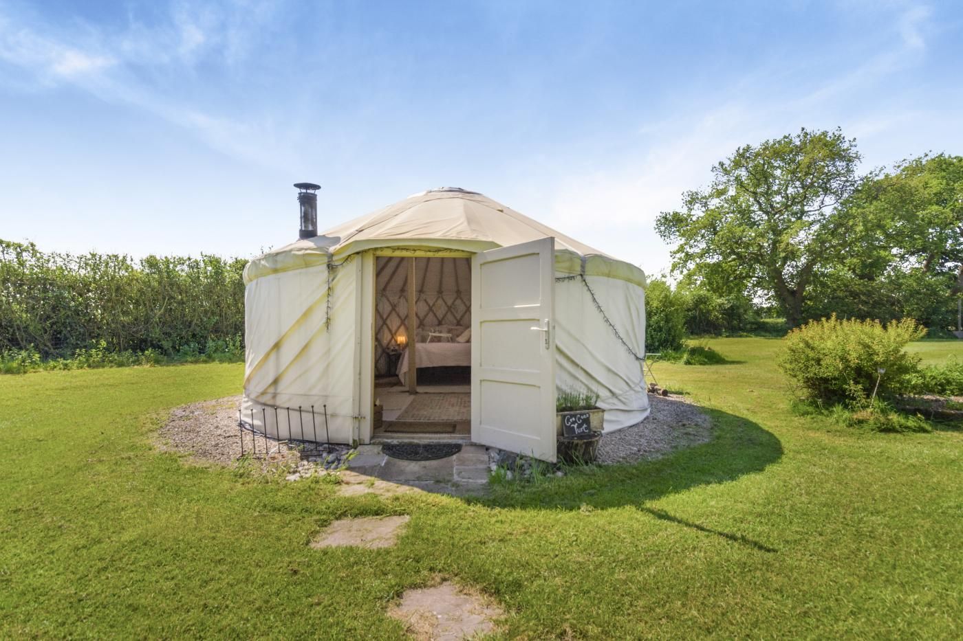 Une yourte avec une entrée ouverte, un lit à l’intérieur et un petit espace extérieur doté d’un foyer.