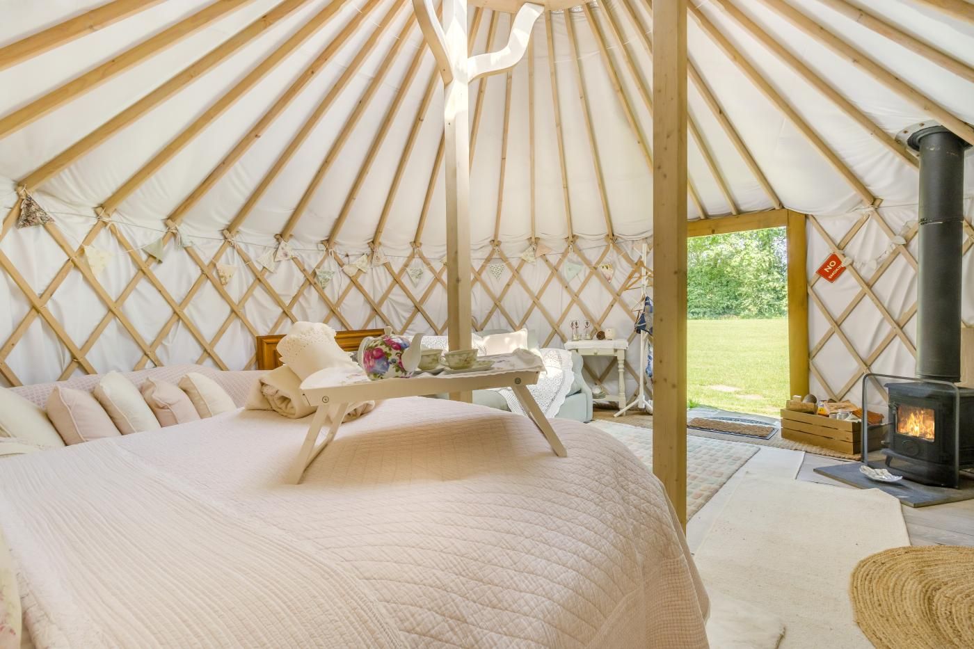 L’intérieur chaleureux d’une yourte, avec un lit, une table où est disposé un service à thé et un poêle à bois.