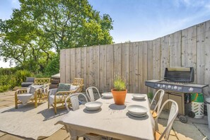 An outdoor patio with a table set for dining, a grill, wicker chairs, and a wooden fence. - 1 Bed in Bronington (oc-g39074) (Bronington)