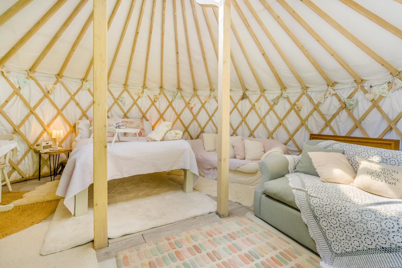 L’intérieur chaleureux d’une yourte, avec un lit, un canapé et une petite table sur laquelle se trouve une lampe.