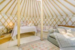 A cozy interior of a yurt with a bed, a sofa, and a small table with a lamp.