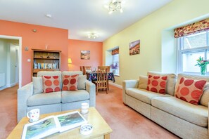 A living room with two sofas, a coffee table with magazines, a bookshelf, and a dining area with a table and chairs. - 2 Bed in Portinscale (oc-lr184) (Portinscale)