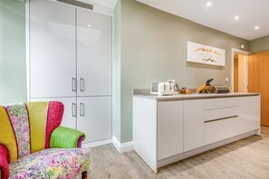 A modern kitchen with white cabinets, a countertop, and a toaster. There is a colorful chair with a floral pattern. - 2 Bed in Portinscale (oc-lr184) (Portinscale)