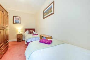 A hotel room with two beds, a wooden wardrobe, a nightstand with a lamp, and a framed picture on the wall. - 2 Bed in Portinscale (oc-lr184) (Portinscale)