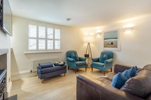A living room with a brown leather sofa, two blue armchairs, a blue ottoman, a floor lamp, and a painting on the wall. - 2 Bed in Fowey (oc-s42445) (Fowey)