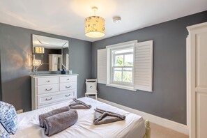 Et soveværelse med seng, kommode, spejl, et vindue med lukker og en loftlampe.