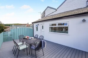 A deck with a table and chairs, a white building with a window, and a blue fence. - 2 Bed in Fowey (oc-s42445) (Fowey)