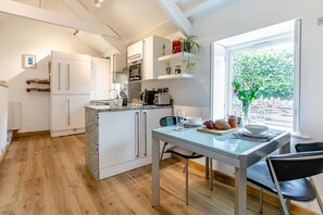 Una cocina moderna con armarios blancos, encimera de granito y comedor con mesa y sillas de vidrio.