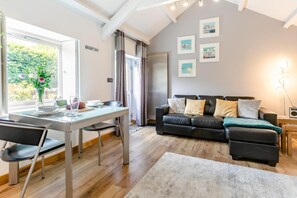 Ein modernes Wohnzimmer mit Essbereich, einer schwarzen Ledersofa und einem großen Fenster mit Vorhängen.