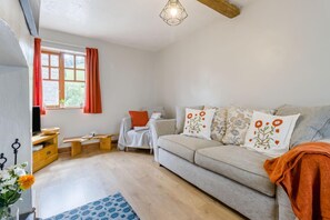 Ein gemütliches Wohnzimmer mit einer Couch, einem Fernseher, einem Holztisch und einem Fenster mit Vorhängen.