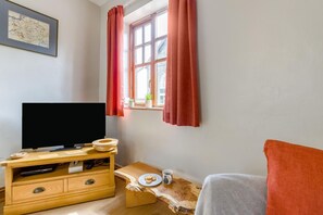 Una habitación con televisión sobre un mueble de madera, una ventana con cortinas rojas, una mesita con un plato y una taza, y un mapa enmarcado en la pared.
