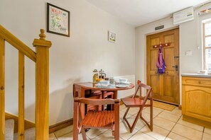Un comedor con una mesa y sillas de madera, un cuadro en la pared y una puerta de madera con un abrigo colgado.