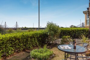 Eine Terrassenfläche mit Tisch und Stühlen, umgeben von Grünpflanzen und einer entfernten Aussicht auf Stromleitungen.