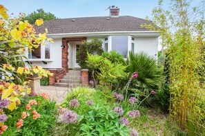 A house with a brick facade, a tiled roof, and a front garden with various plants and flowers. - 2 Bed in Wells (oc-s41752) (Wells)