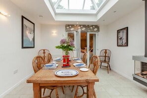 A dining area with a wooden table set for four, a vase of flowers, and a view of a bedroom through an open door. - 2 Bed in Wells (oc-s41752) (Wells)