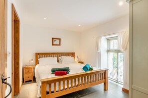 Een slaapkamer met een houten bed, witte beddengoed, een nachtkastje, een bedlampje en een raam met gordijnen.