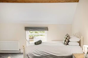 Un dormitorio con cama, ventana con vistas, radiador y techo de madera.