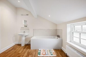 Ein modernes Badezimmer mit einer freistehenden Badewanne, einem Standwaschbecken und einem Fenster mit Milchglas.