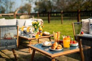 Ein Essbereich im Freien mit einem Tisch, der für ein Frühstück gedeckt ist, darunter Croissants, Obst und Getränke.