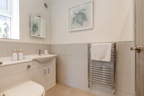 Ein Badezimmer mit einem weißen Waschbecken, einer Toilette, einem Handtuchhalter und einem Bild einer gerahmten Meeresschildkröte an der Wand.