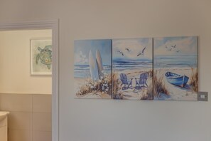 A wall with three paintings depicting beach scenes, including chairs, a boat, and surfboards. - 3 Bed in Bournemouth (oc-s44899) (Bournemouth)