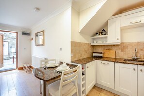 A modern kitchen with white cabinets, granite countertops, and a dining area with a table set for four. - 1 Bed in Beadnell (oc-a45438) (Beadnell)