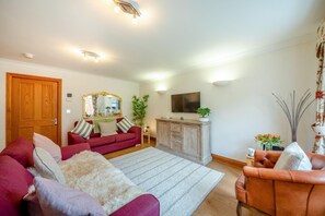 A living room with a red sofa, a white furry rug, a wooden cabinet, and a TV mounted on the wall. - 1 Bed in Beadnell (oc-a45438) (Beadnell)