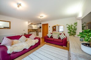 A living room with a red sofa, a white furry throw, and a wooden coffee table. There is a kitchen visible through an open door. - 1 Bed in Beadnell (oc-a45438) (Beadnell)