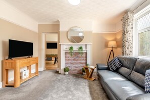 Ein Wohnzimmer mit Fernseher, Holzschrank, Ledersofa und Kamin mit Pflanzen.